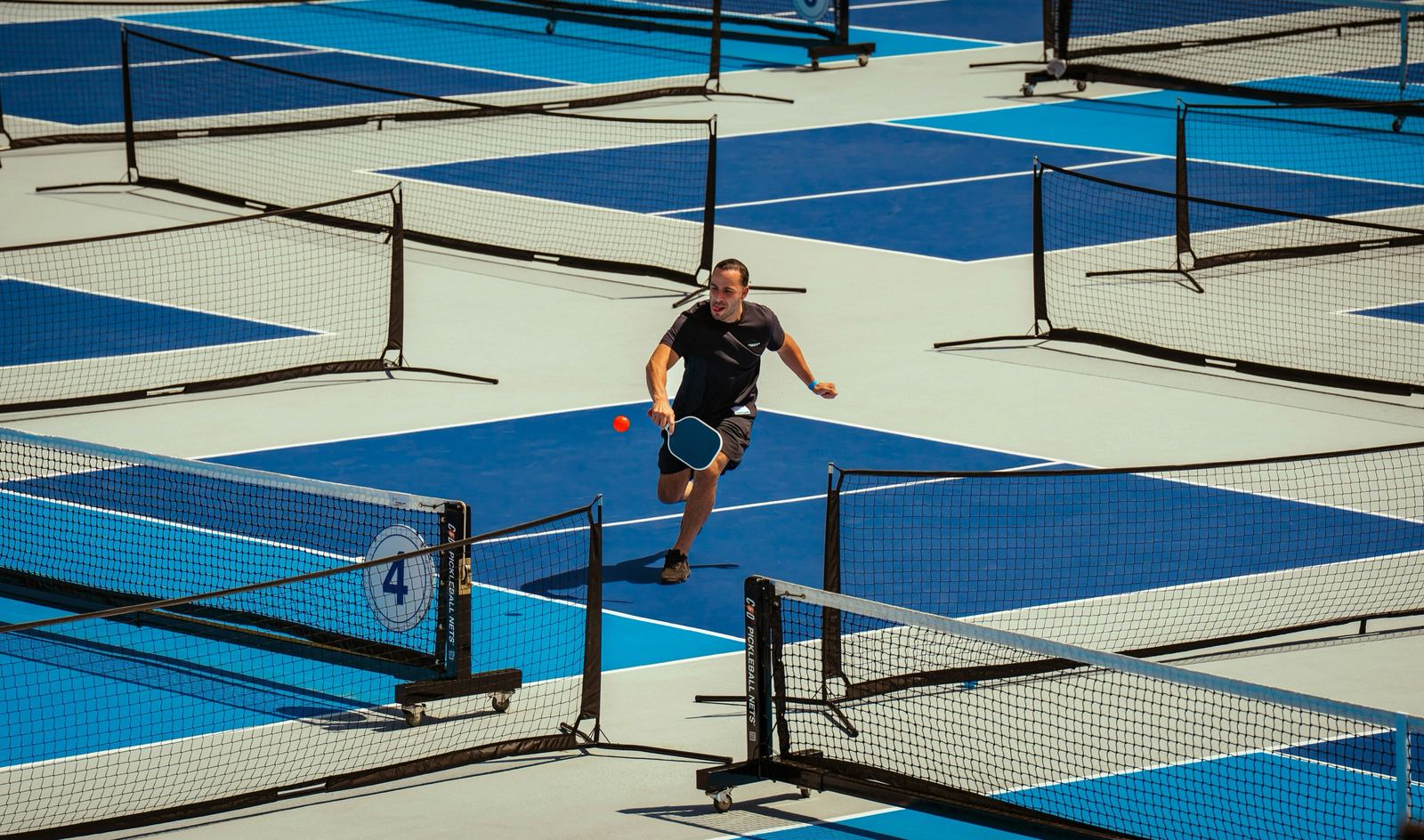 A ladder league in progress across a row of blue pickleball courts