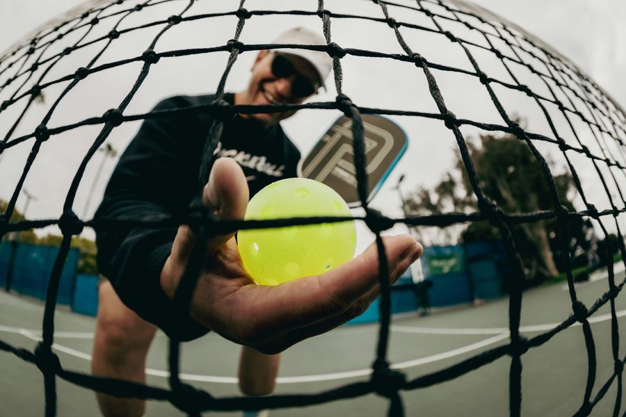 A player holding a pickleball up to the camera through the net