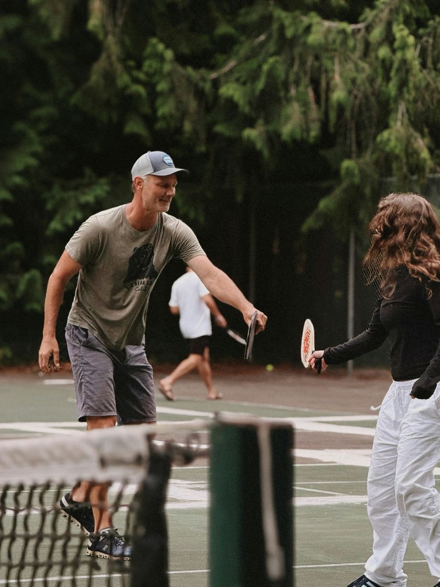 Two players trading shots at the net on a tree-lined court